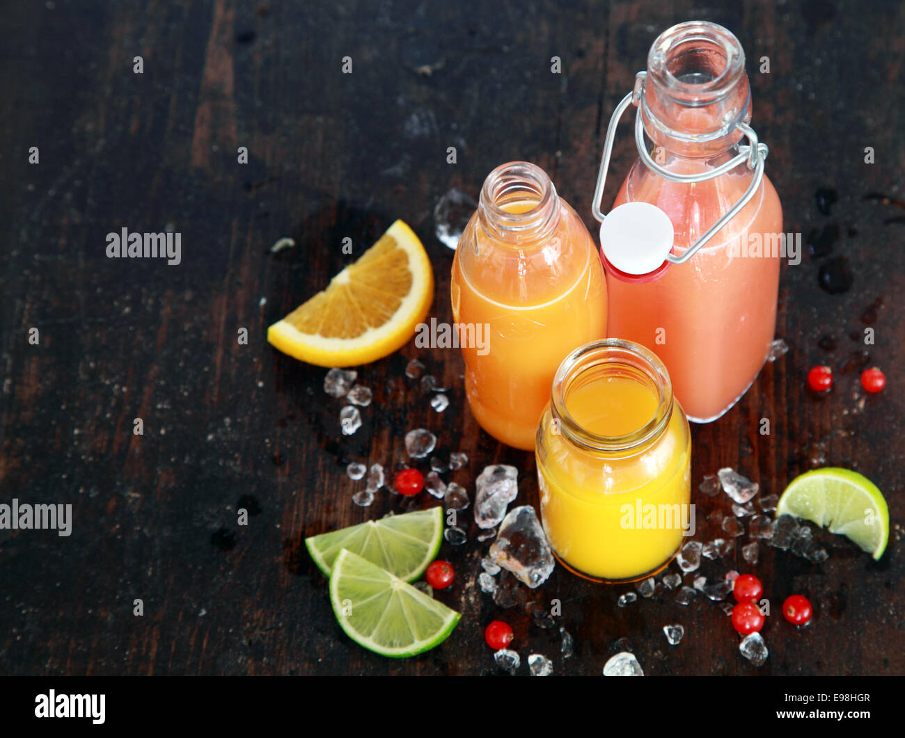 Vorbereitung leckeren gesunden Sommer Fruchtsäfte in Glasflaschen mit Scheiben von frischem Orange, Zitrone, Limette und Preiselbeeren, hoher Winkel auf eine dunkle rustikale Holzoberfläche mit Exemplar angesehen Stockfoto