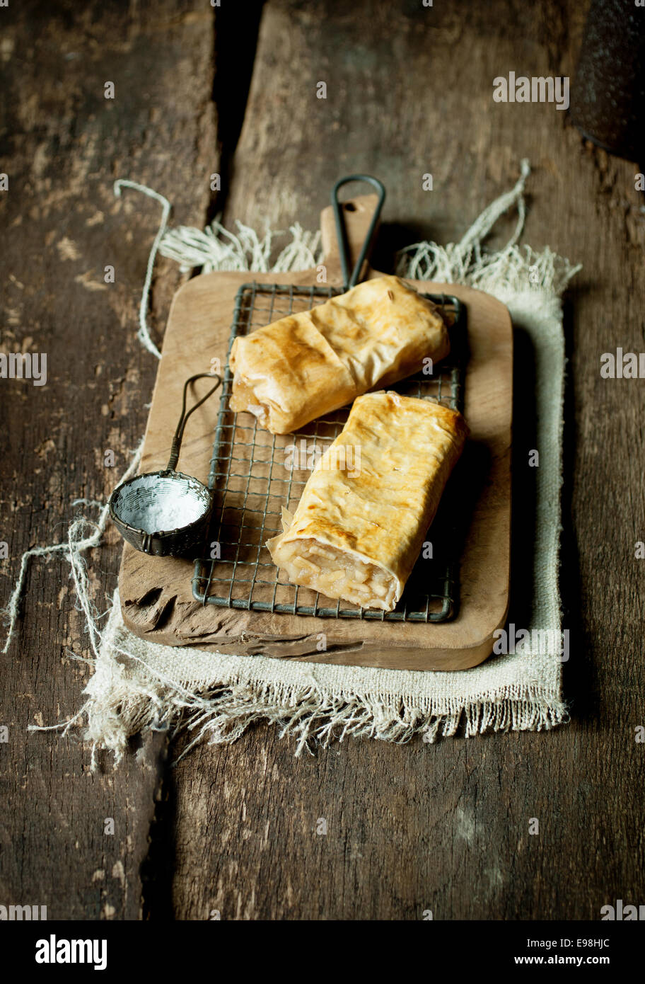 Zwei gebackene frisch leicht schuppige deutschen Apfelstrudel oder Apple Strudel serviert auf einem Vintage alten rustikalen Holzbrett mit einem Sieb Puderzucker darüber streuen Stockfoto