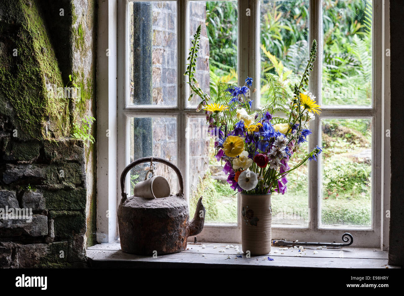 The Lost Gardens of Heligan, Cornwall, Großbritannien. Ein alter Wasserkocher und eine Vase mit Schnittblumen auf dem Fensterbrett eines Gartenhäuschens Stockfoto