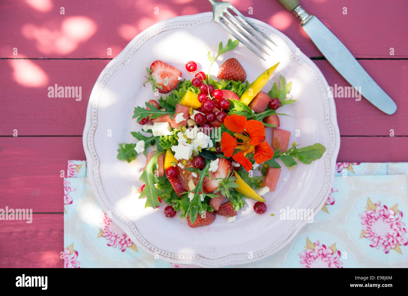 Leckeren Sommersalat Melone, Erdbeeren, Johannisbeeren und wilde Blumen auf rosa Hintergrund aus Holz Stockfoto