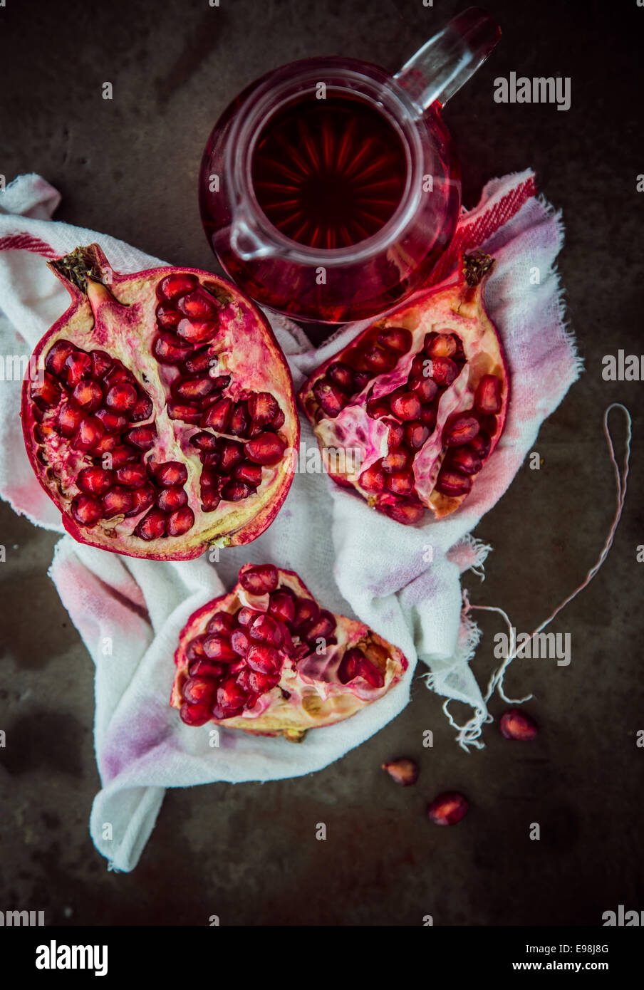 Herstellung frischer Granatapfelsaft mit einem Overhead einer gebrochenen offenen Frucht anzeigen die reifen roten Samen auf einem gefärbten Baumwolltuch mit einem Krug frisch zubereitete Saft neben anzeigen Stockfoto