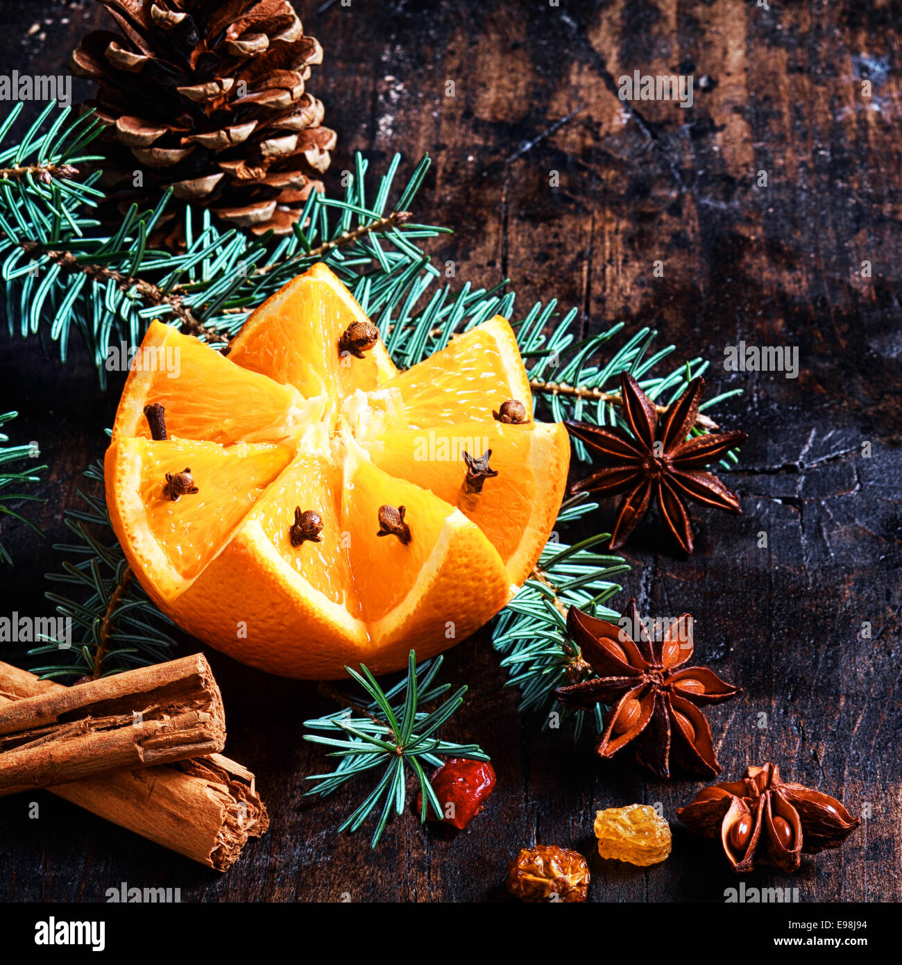 Weihnachten-Frucht und Würze-Hintergrund mit einem bunten Muster geschnitten Orange dekoriert mit Nelken eingebettet auf Kiefer Laub mit einem Kegel, Zimt, Sternanis und Muttern auf einer rustikalen Kulisse im quadratischen format Stockfoto