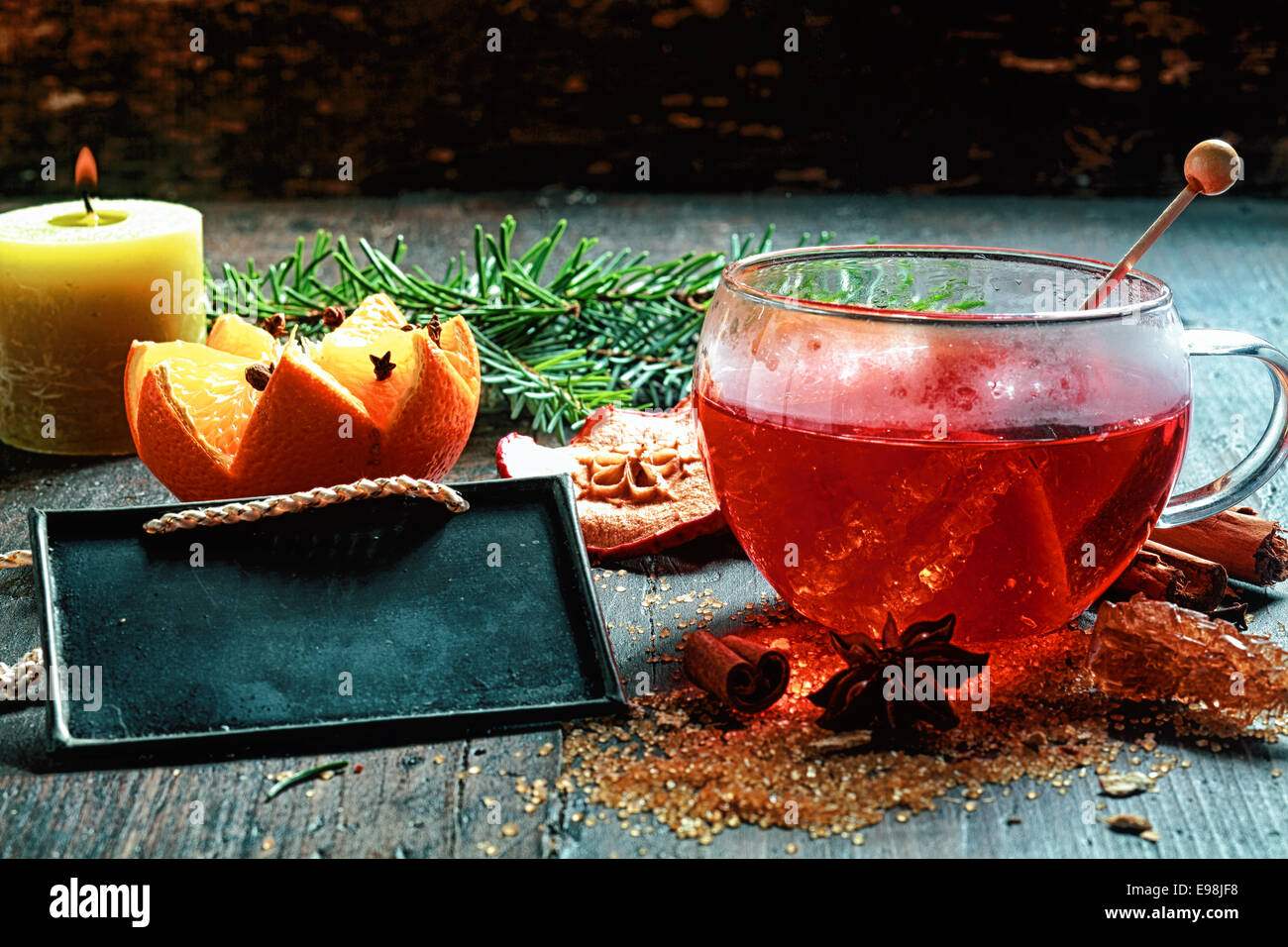 Heiligabend gewürzt, heißen Tee oder Glühwein mit kristallisierter Zucker, eine dekorative Orange und Gewürze neben einer brennenden Kerze und Stockfoto