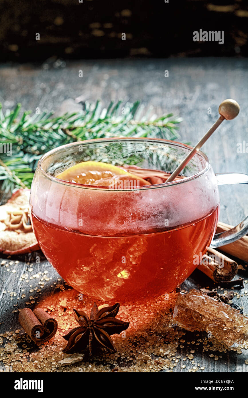 Heiße Tasse würzigen heißen Tee oder Glühwein mit Kristallzucker Rührer und Zitrusfrüchten umgeben von getrocknetem Zimt, Sternanis und karamellisierten Zucker auf einem rustikalen Weihnachten Hintergrund mit Exemplar Stockfoto