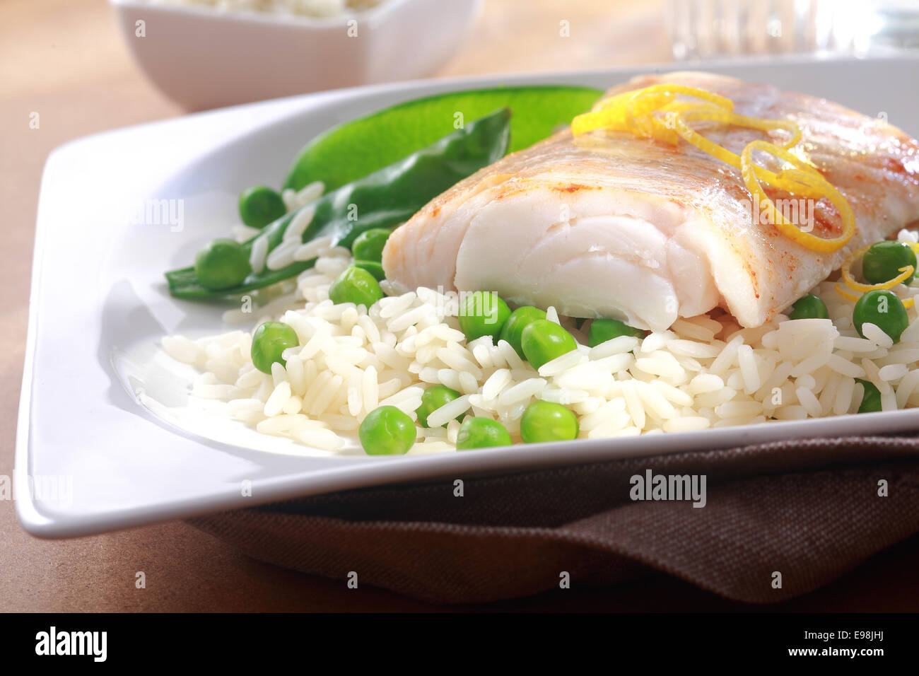 Gebackenes Fischfilet, garniert mit frischer Zitronenschale, Reis und Erbsen gesund essen, auf einem weißen Teller Stockfoto