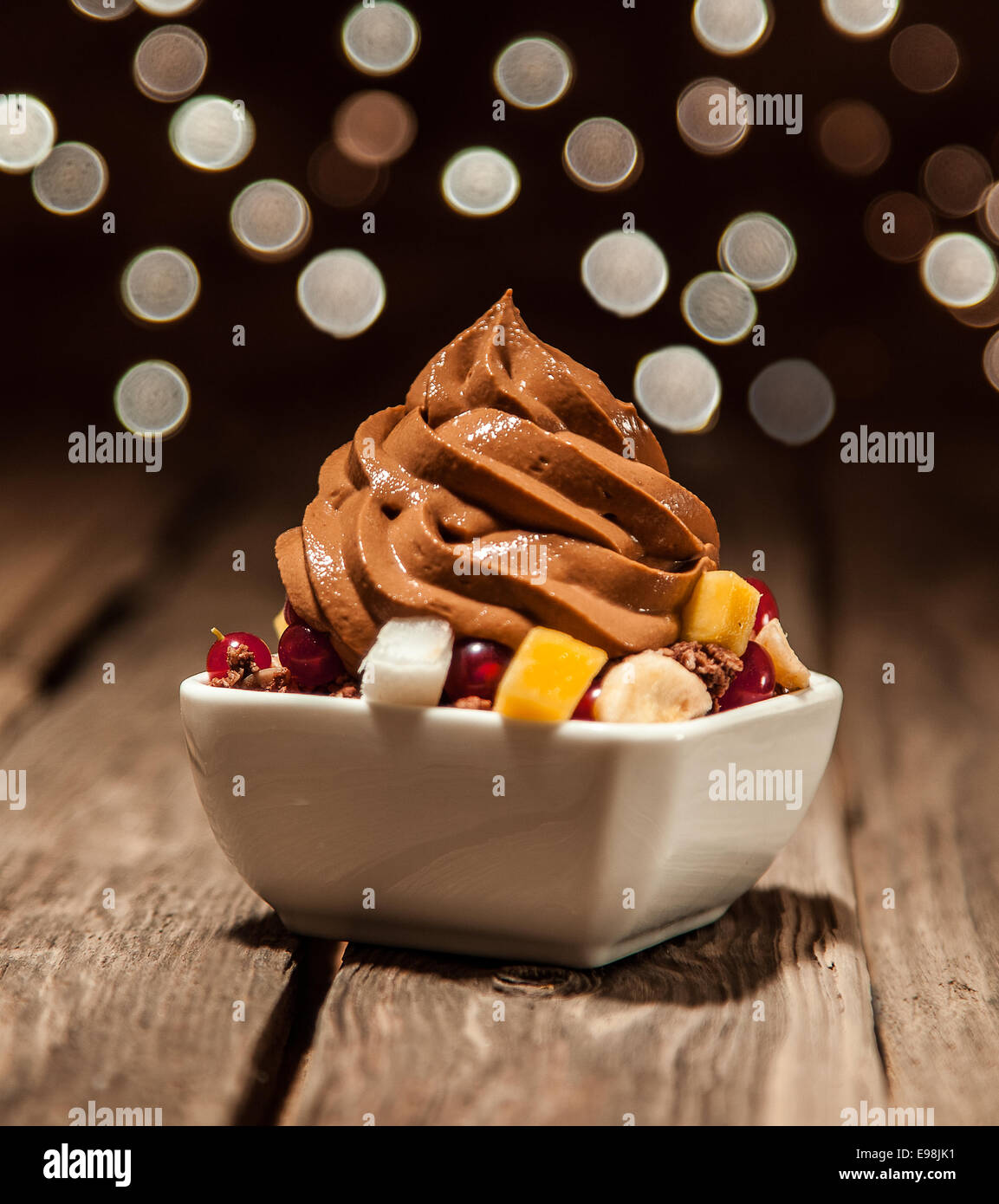 Nahaufnahme Brown Frozen Joghurt oben geschnitten Früchte auf Schüssel auf Holztisch gelegt. Stockfoto