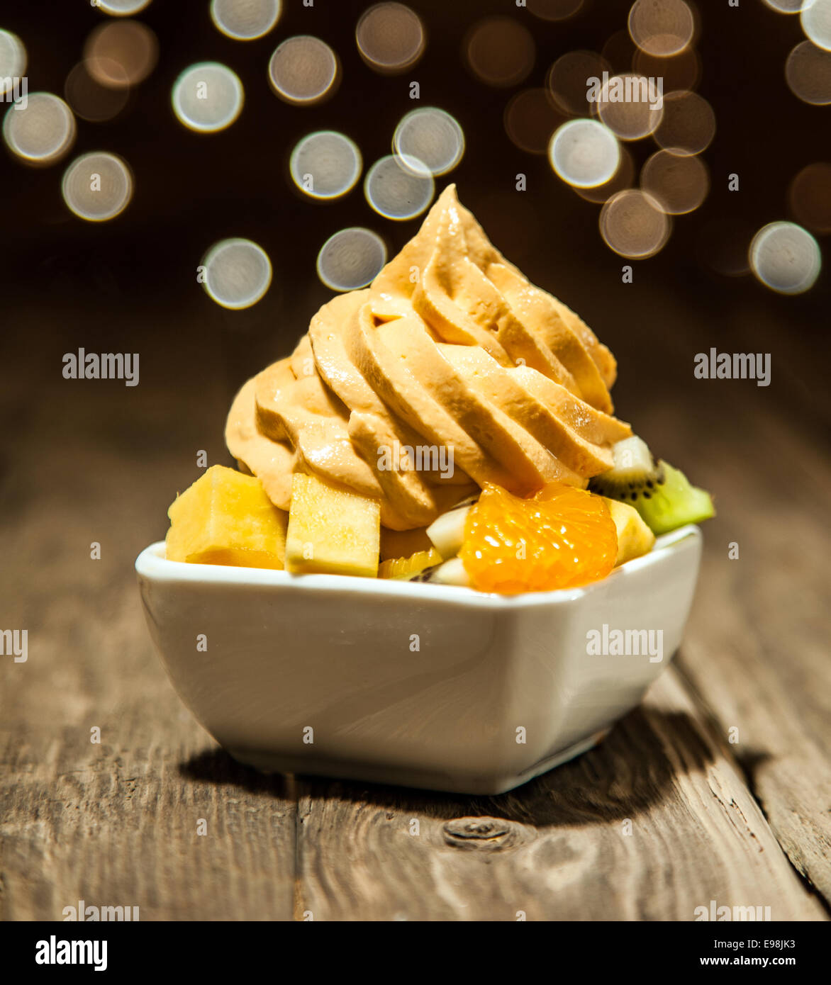 Makro Munde gelbe gefrorenen Joghurt auf verschiedene FRUCHTSCHEIBEN auf weiße Schüssel auf Holztisch gelegt. Stockfoto