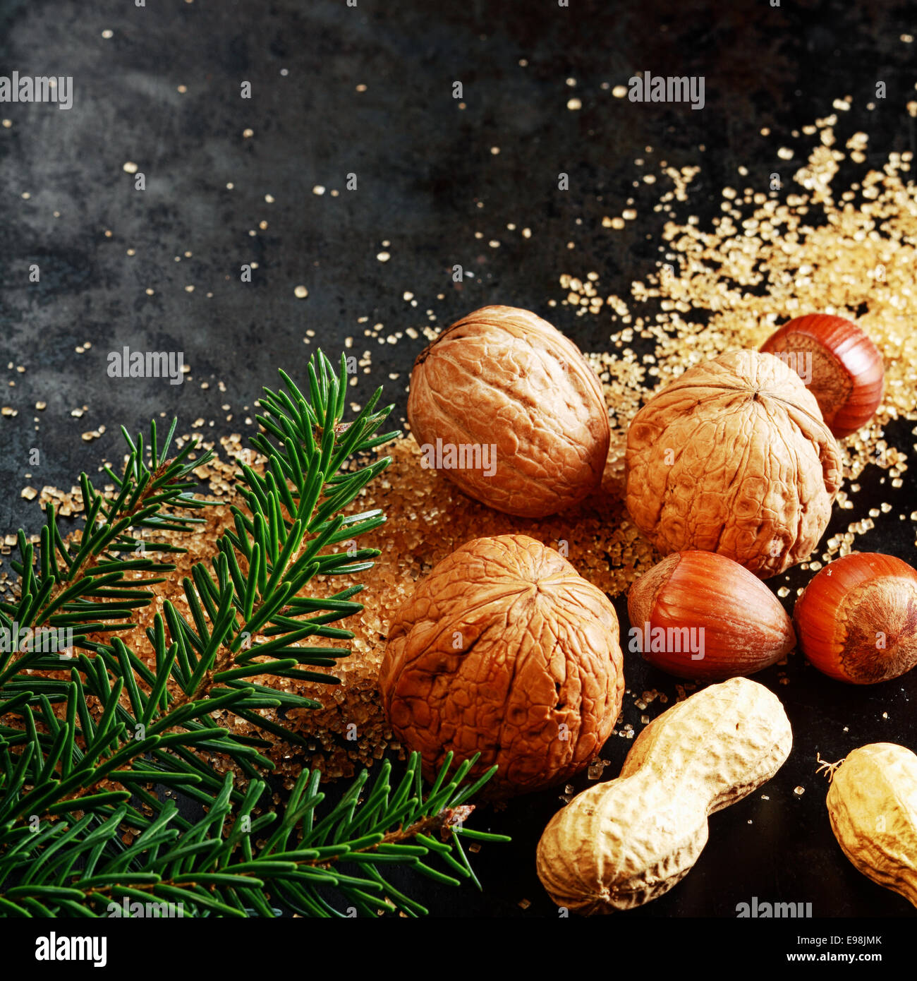 Frisch sortiert ganze Nüssen für eine festliche Weihnachten mit Mandeln, Haselnüsse und Erdnüsse in der Schale auf braunen karamellisierten Zucker mit Kiefer Laub auf einem dunklen Hintergrund mit Exemplar für Ihre Ansage Stockfoto