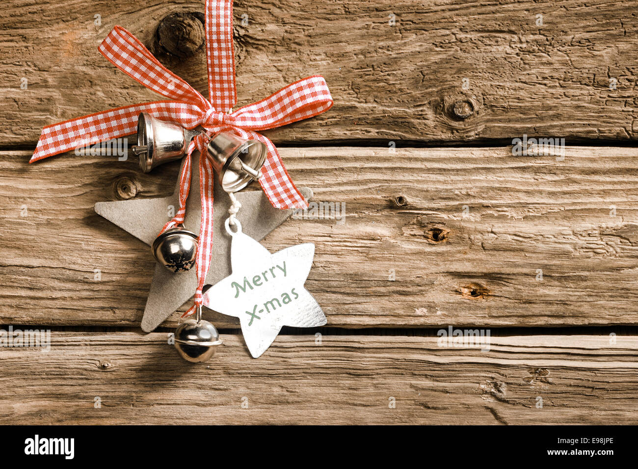 Ein Land feiert überprüft Weihnachten mit dekorativen Sternen und Silberglocke Habging aus ein rot-weißes, Band und Schleife am rustikalen Holzbretter mit einem sternförmigen Tag mit der Meldung - Frohe Weihnachten Stockfoto