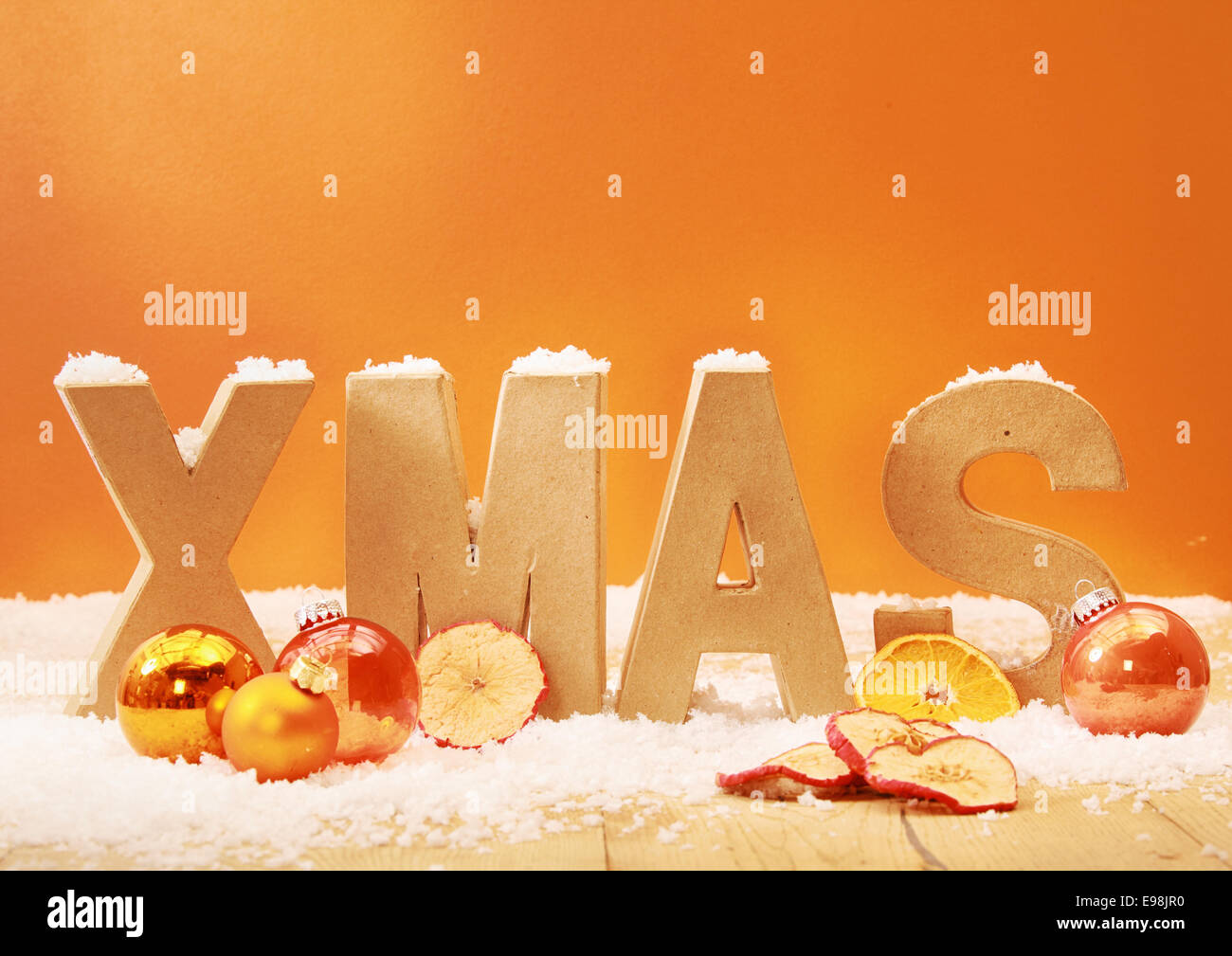 Warm getönten Weihnachten Hintergrund mit Holzbuchstaben für Weihnachten im Schnee mit orange und goldenen Verzierungen und getrockneten Apfel und Orangenscheiben gegen einen orange Hintergrund mit Exemplar Stockfoto