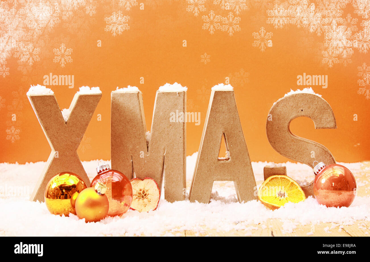 Bunte Weihnachten Hintergrund mit fallenden Schneeflocken und hölzernen Buchstaben Xmas bedeckt im Schnee mit Orange und goldenen Verzierungen und Obst an einem warmen getönten orangefarbenen Hintergrund Stockfoto