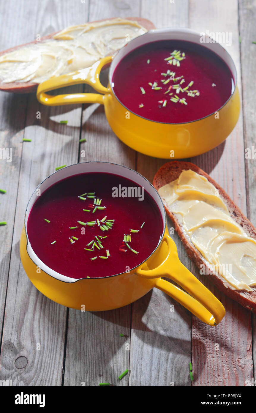 Appetitliche rote Bete Suppe in gelbe Schale mit Griff, mit geschnittenem Brot auf Seiten, die auf hölzernen Tisch platziert. Stockfoto