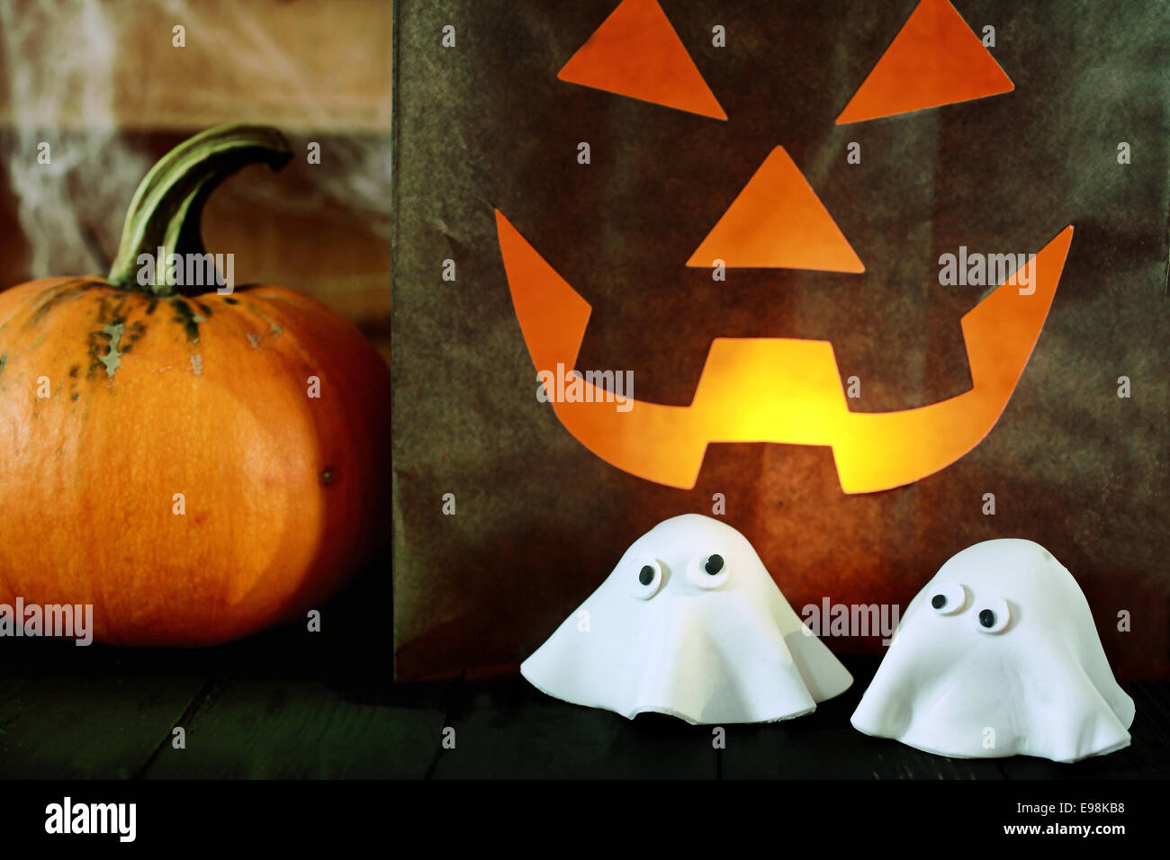 Scary Halloween Party Hintergrund mit einem glühenden Papier Tasche Jack-o-Laterne mit einem teuflischen Gesicht neben einem frischen Kürbis und niedlichen beängstigend kleine Geister gemacht, der Teig für einen kreativen snack Stockfoto