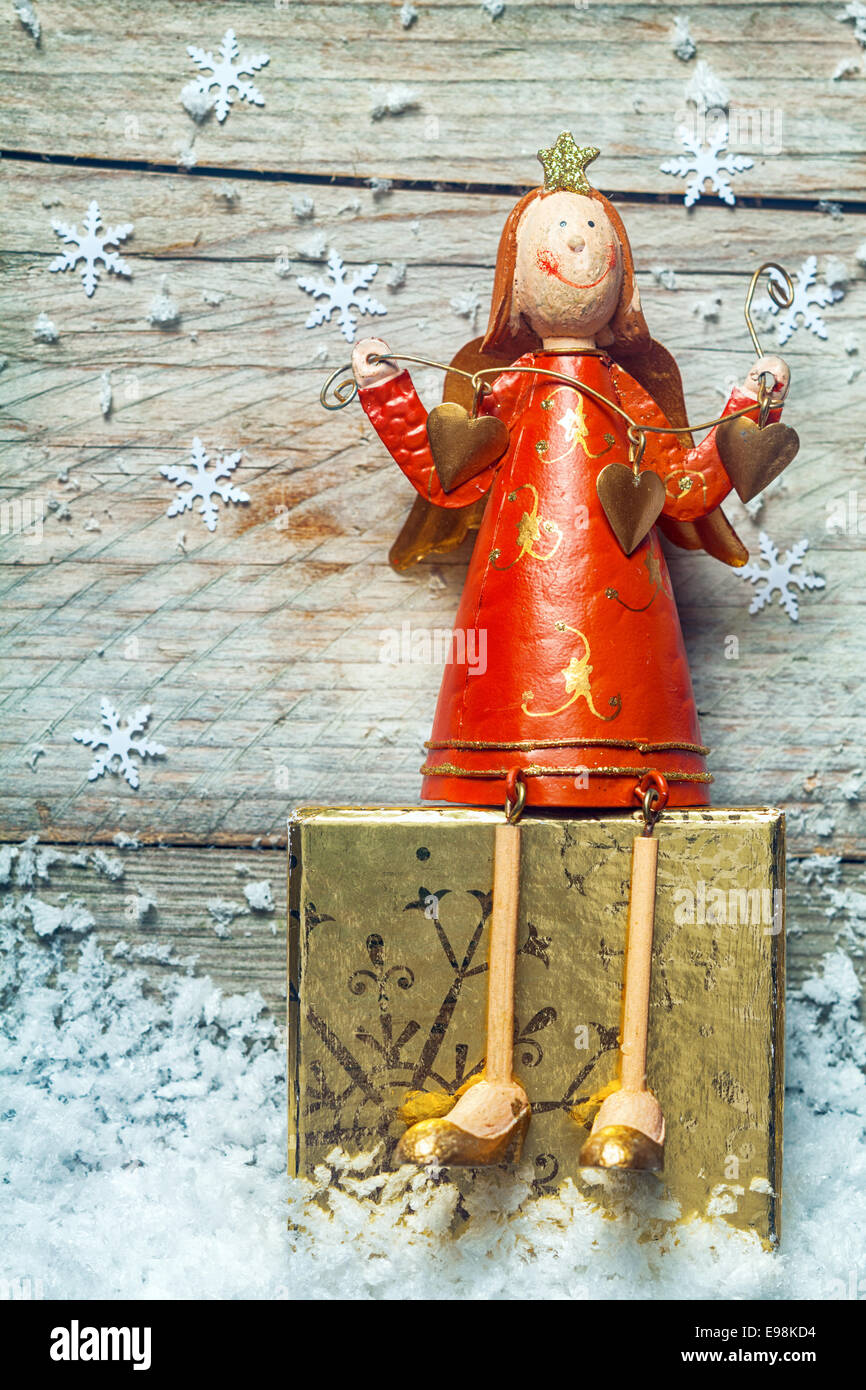 Niedliche Retro-Stil aus Holz Weihnachtsengel in einem bunten roten Kleid sitzt auf einem dekorierten gold-Block eingebettet in Schnee fallen Stockfoto