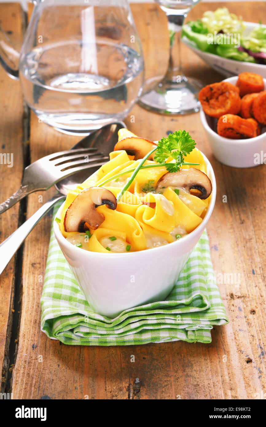 Rustikaler Holztisch Einstellung mit einer Schüssel mit frisch zubereiteten Pilz Tagliatelle und Salat-Beilagen Stockfoto