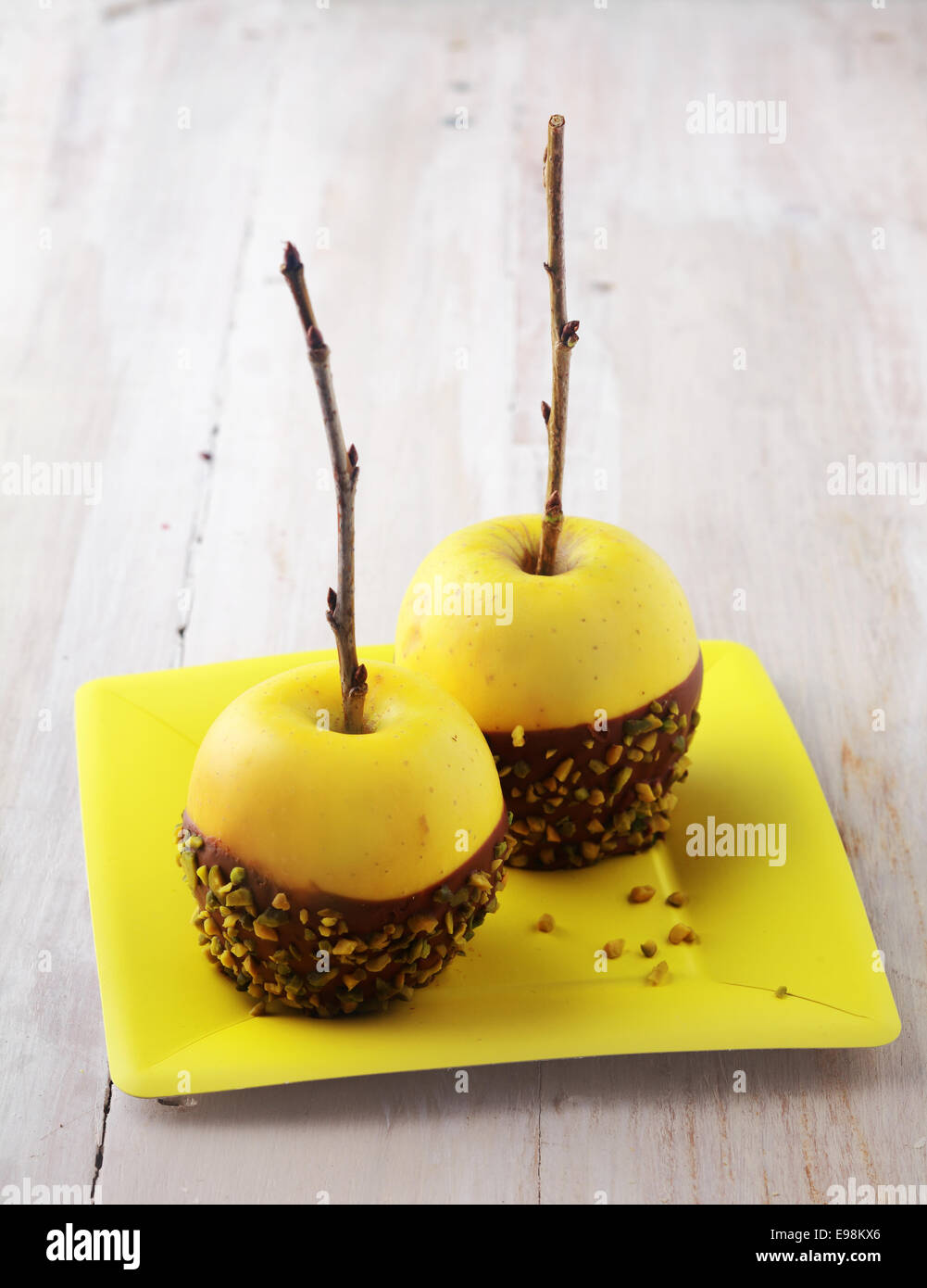 Gesunde frische Bio goldenen gelbe Äpfeln dekoriert mit Schokolade und gehackten Nüssen serviert auf eine quadratische gelbe Platte für ein Halloween-Dessert, rustikale Tafel Hintergrund mit Exemplar Stockfoto