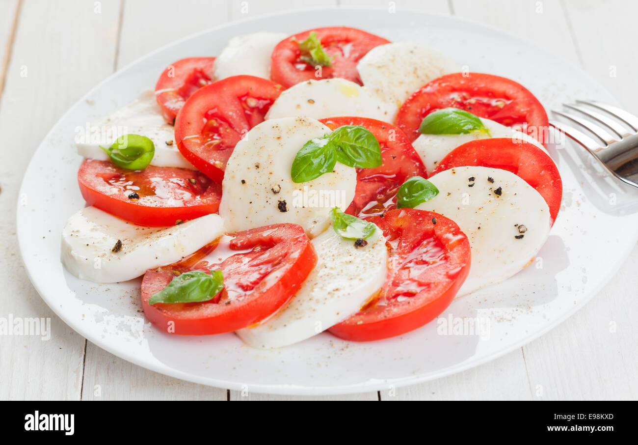 Italienische Caprese Salat mit bunten rote Tomate und weißem Mozzarella Scheiben abwechselnd gewürzt mit Salz und Pfeffer und frischem Basilikum Blätter Stockfoto
