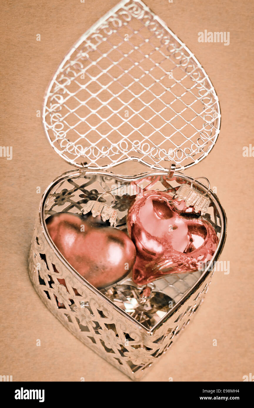 Valentinstag oder Jahrestagsgeschenk für romantische Herzen eingebettet in einer silbernen filigranen herzförmigen Geschenkbox Stockfoto