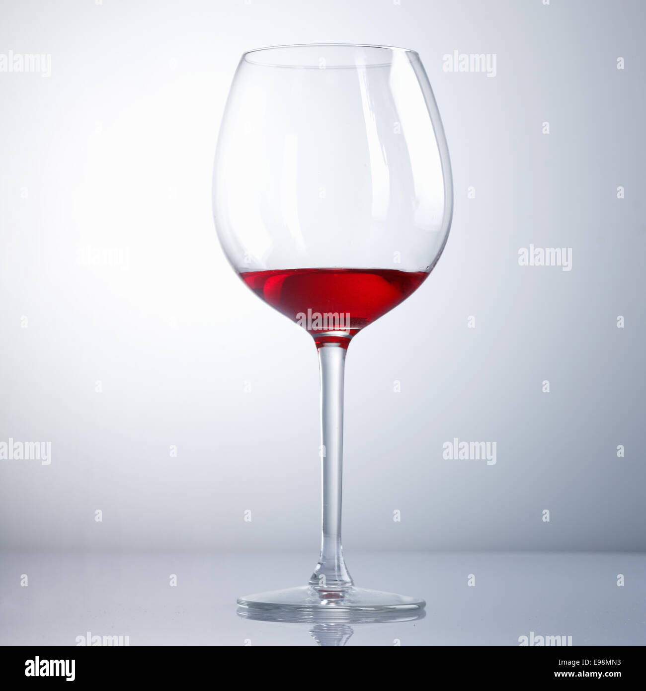 Halb betrunken Weinglas auf einem hellblauen Hintergrund mit Überlegung Stockfoto