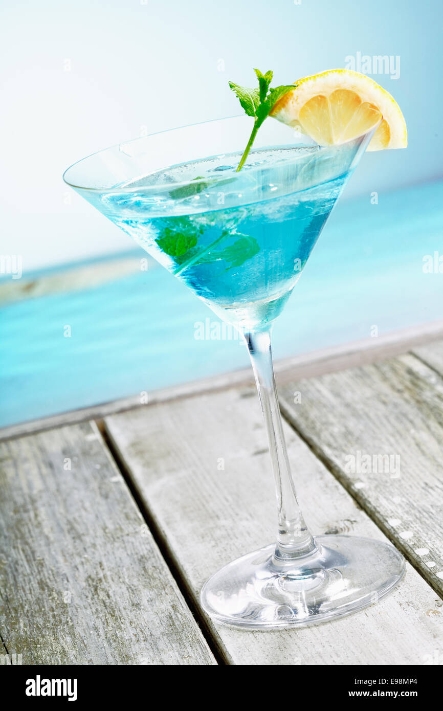 Erfrischende klassische blue Curaçao Martini cocktail mit frischer Zitrone garniert und serviert neben dem Ozean auf einem tropischen Urlaub Stockfoto