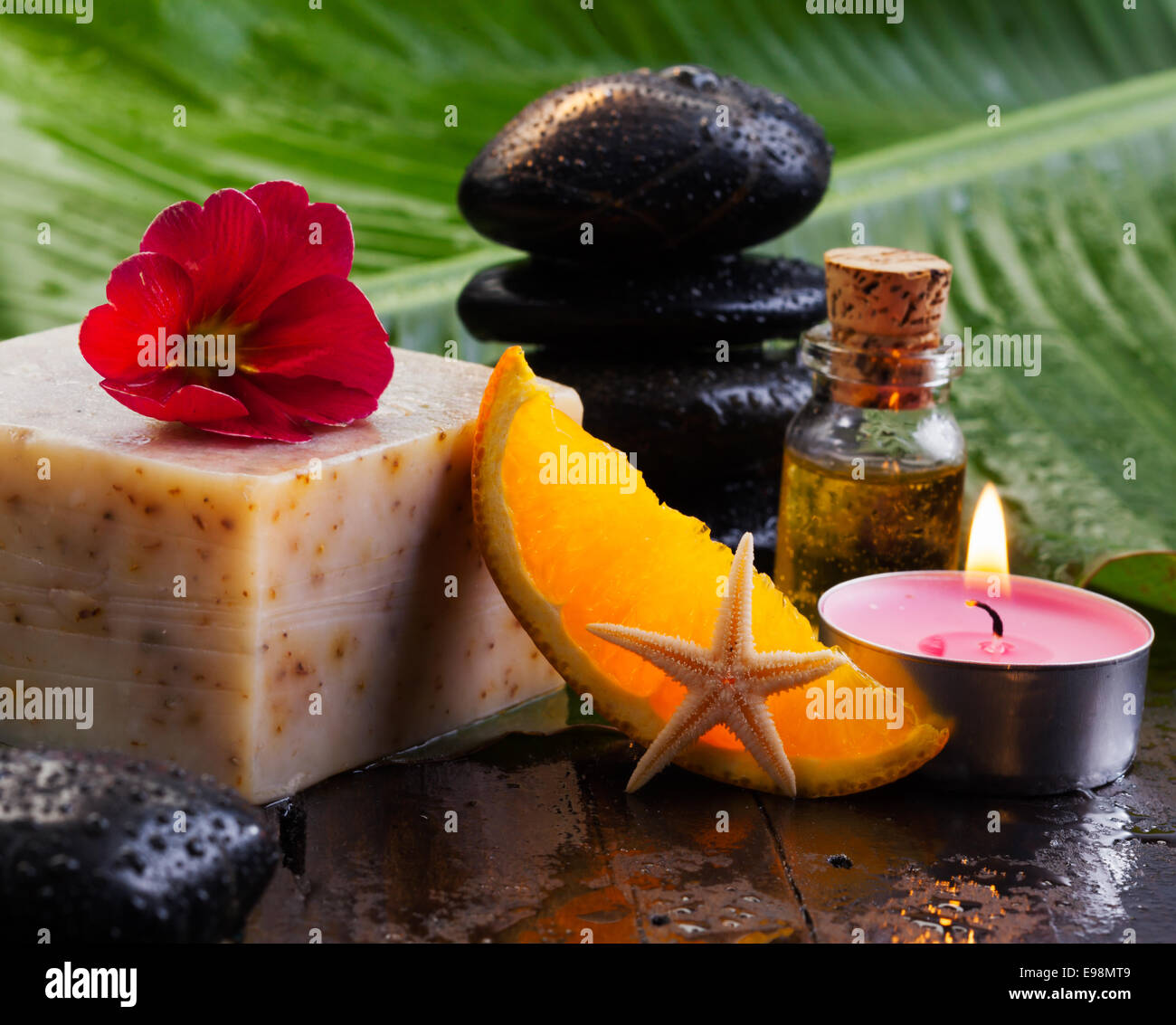 Käse-Block und Orange Slice ruht auf einem Tisch mit Basaltsteinen und Öle für einen Wellnessurlaub Stockfoto