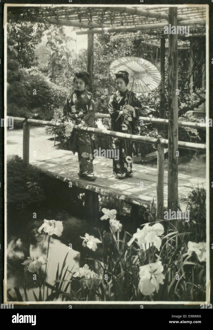 Ein Vintage-Foto von zwei Frauen, möglicherweise Geishas, auf einer japanischen Brücke in einem Garten. Das Bild zeigt traditionelle japanische Mode und Architektur in einer ruhigen Umgebung. Stockfoto