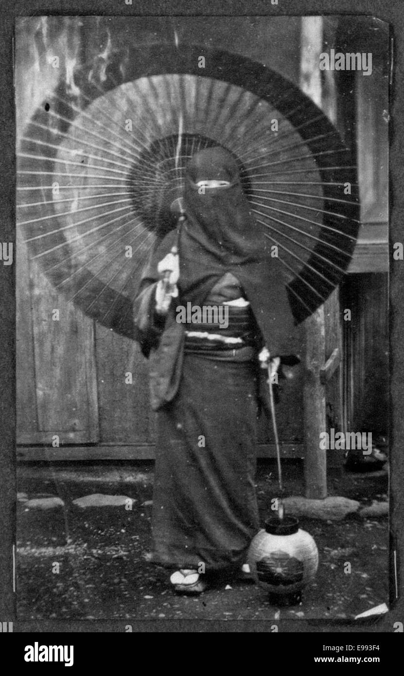 Dieses Foto zeigt eine Frau in Winterkleidung, die in Japan einen Regenschirm hält. Es zeigt eine typische Szene des täglichen Lebens und zeigt die Mode und das Klima der damaligen Zeit in Japan. Stockfoto