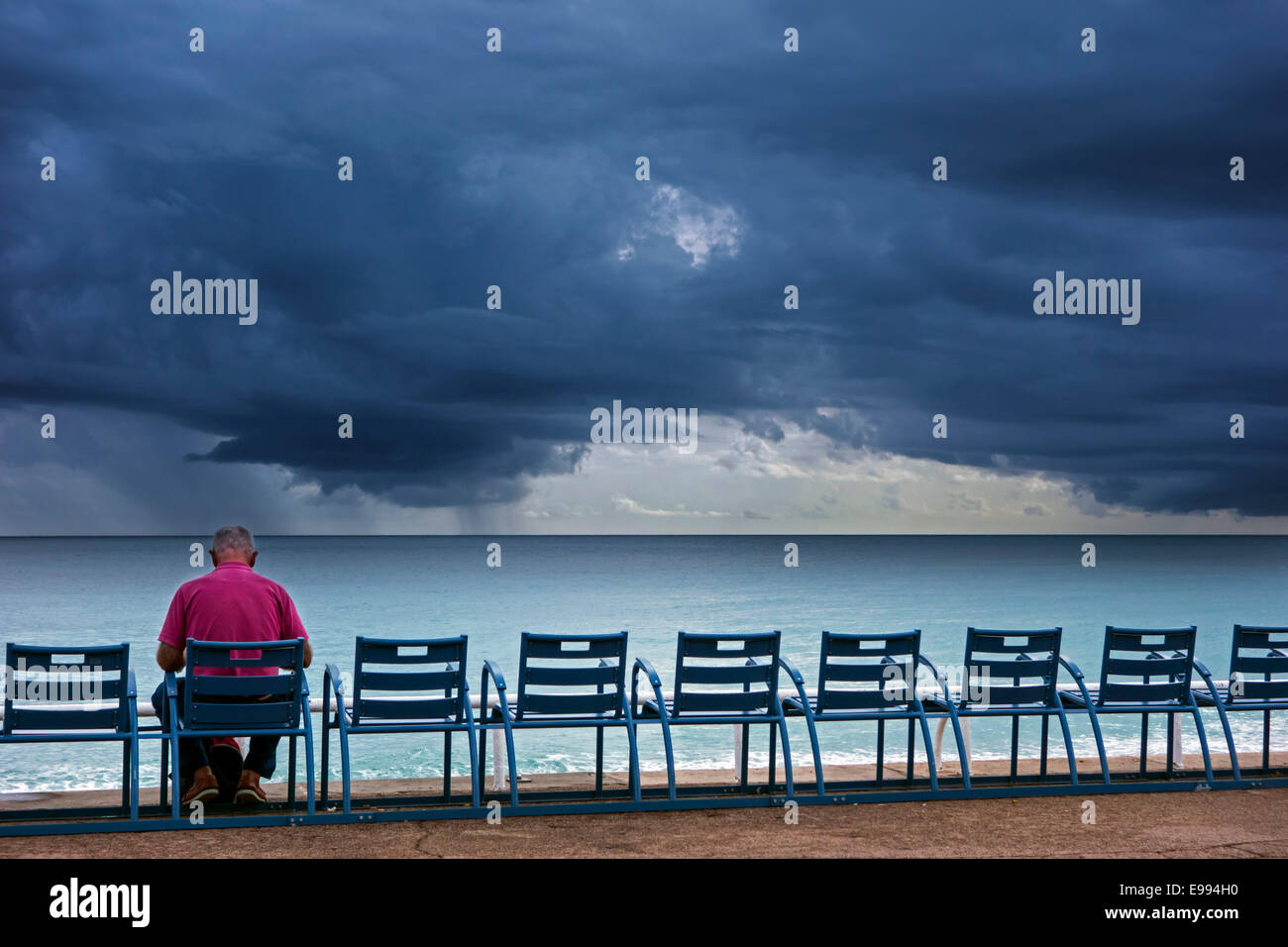 Ältere Mann auf Bank am Deich sitzen und beobachtete dunkle, bedrohliche Gewitterwolken über dem Meer Stockfoto