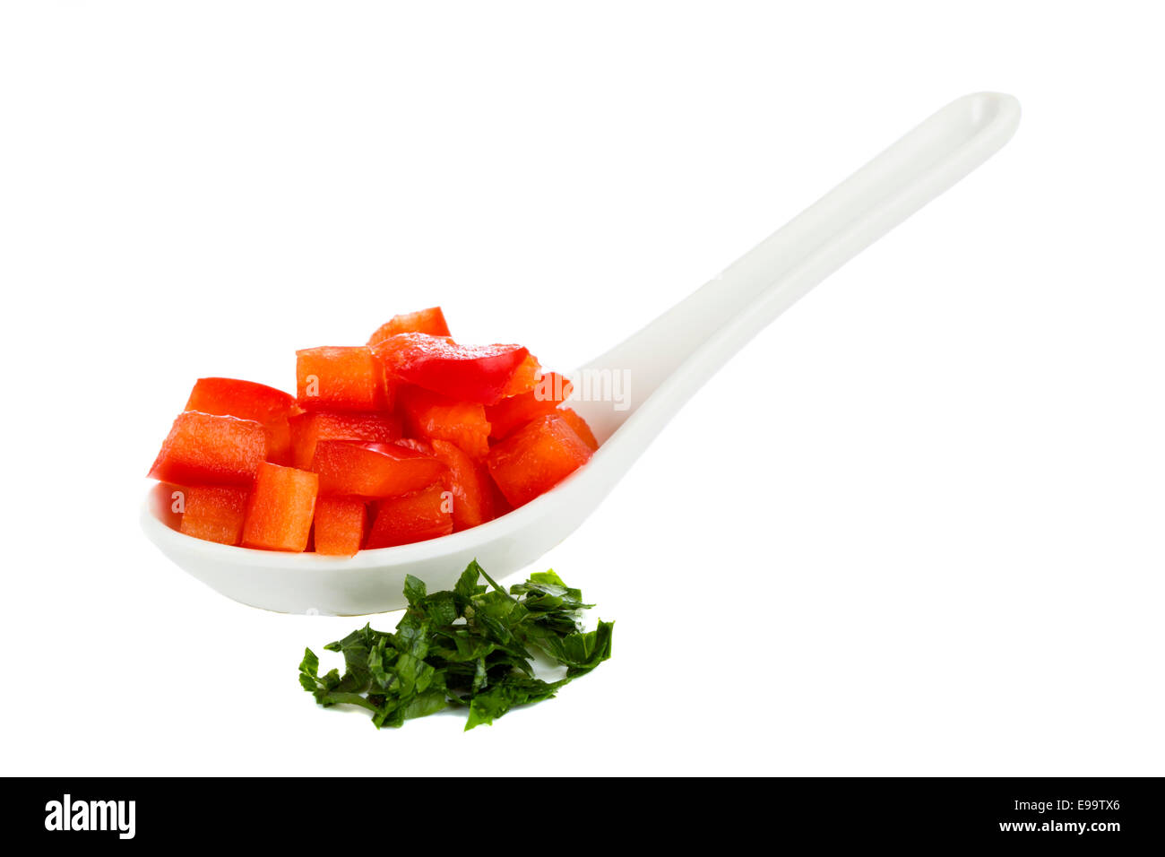 Gehackte rote Paprika in weißen Löffel und gehackte Petersilie isoliert auf weißem Hintergrund Stockfoto