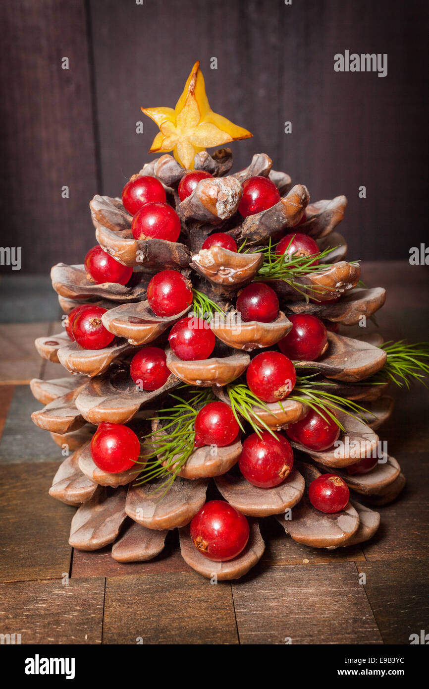 Tannenzapfen dekoriert mit Preiselbeeren als Baum zu Weihnachten auf hölzernen Hintergrund Weihnachtsschmuck von Tannenzapfen und Beeren Stockfoto