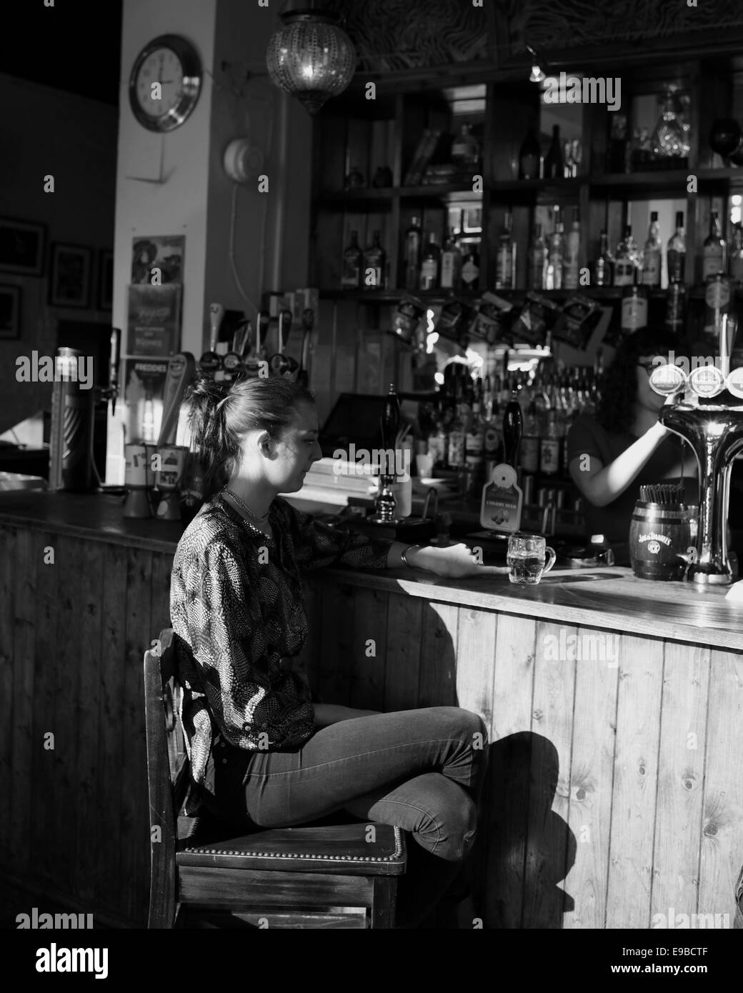 Junge Frau sitzt in einer Bar, sinniert über ihr halbes Pint Bier Stockfoto