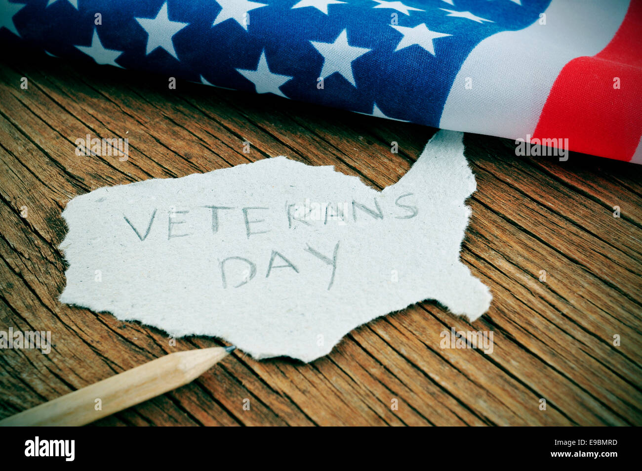 ein Stück Papier in der Form der Vereinigten Staaten mit dem Wort Veterans Day auf einem hölzernen Hintergrund mit der Flagge des Vereinigten Sta Stockfoto