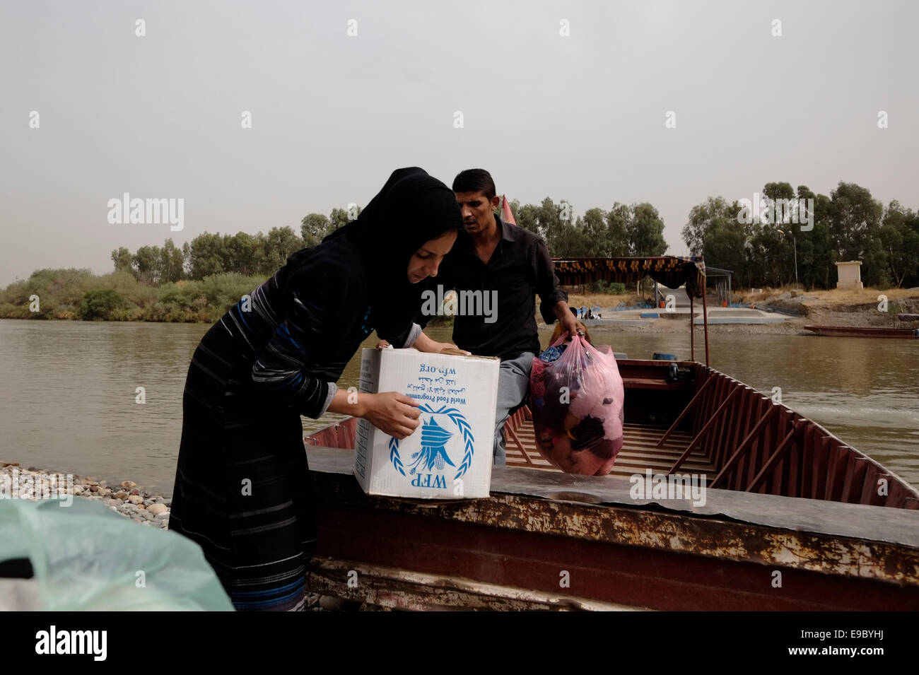 Eine Kurdin trägt eine Kiste mit Lebensmitteln, die vom Welternährungsprogramm der Vereinten Nationen (United Nations World Food Programme) WFP gespendet wurde, nachdem sie den Fluss Tigris auf einem Boot am Grenzübergang Fishkhabur oder Fishkhabur - Semalka von der irakischen Region Kurdistan in Syriens nordöstliches Kurdengebiet überquert hat Stockfoto