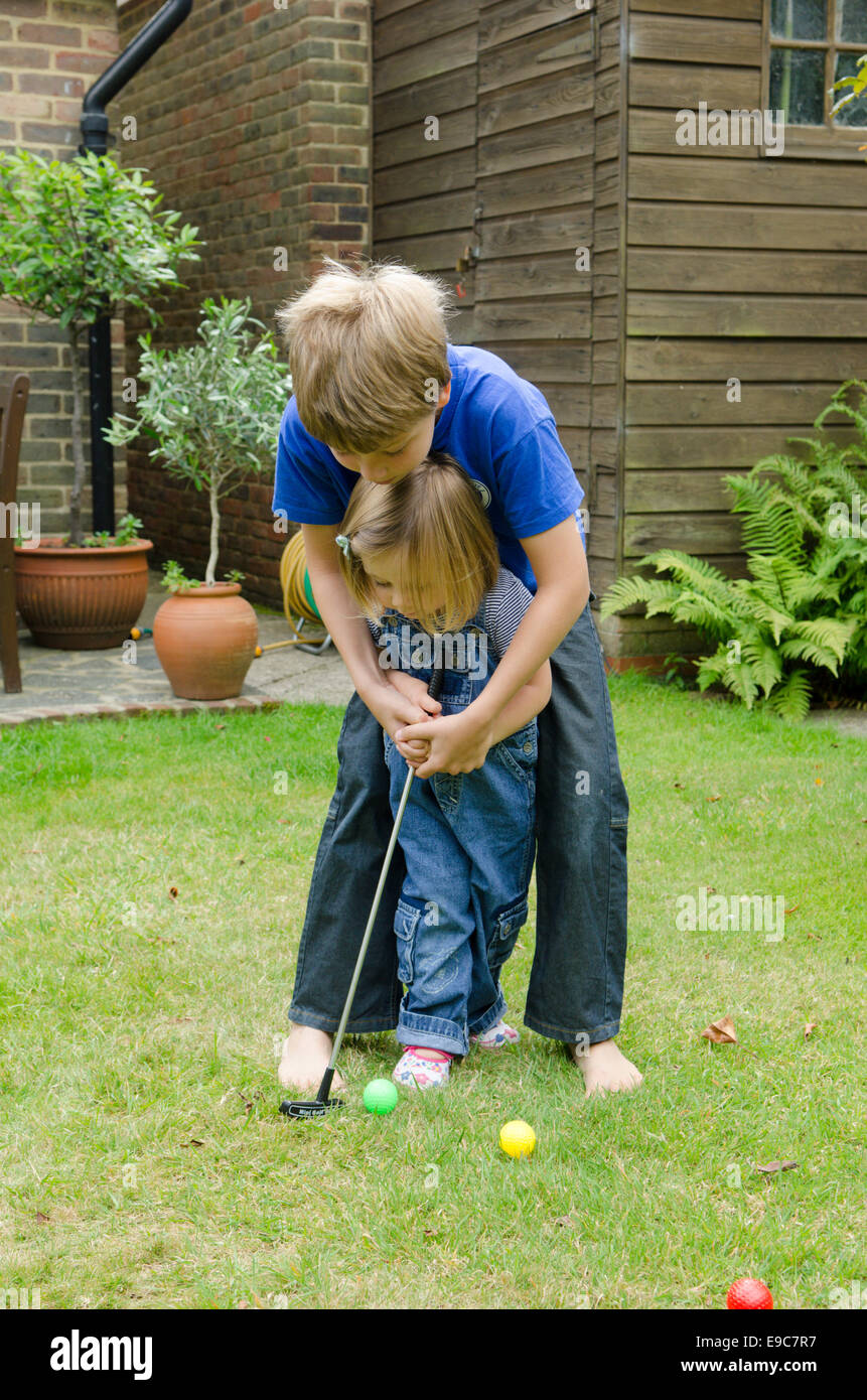 acht Jahre alter Junge Lehre, seine zwei Jahre alten Schwester wie zum Golfspielen im Garten Stockfoto