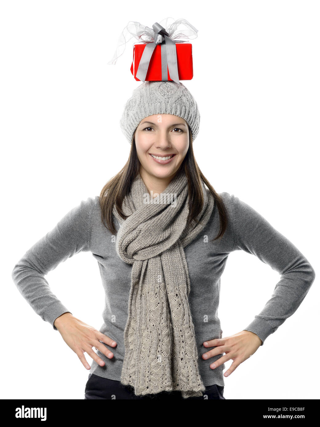Glücklich attraktive junge Frau in Wintermode Ausgleich ein Weihnachtsgeschenk auf ihrem Kopf stehend in die Kamera schaut Stockfoto