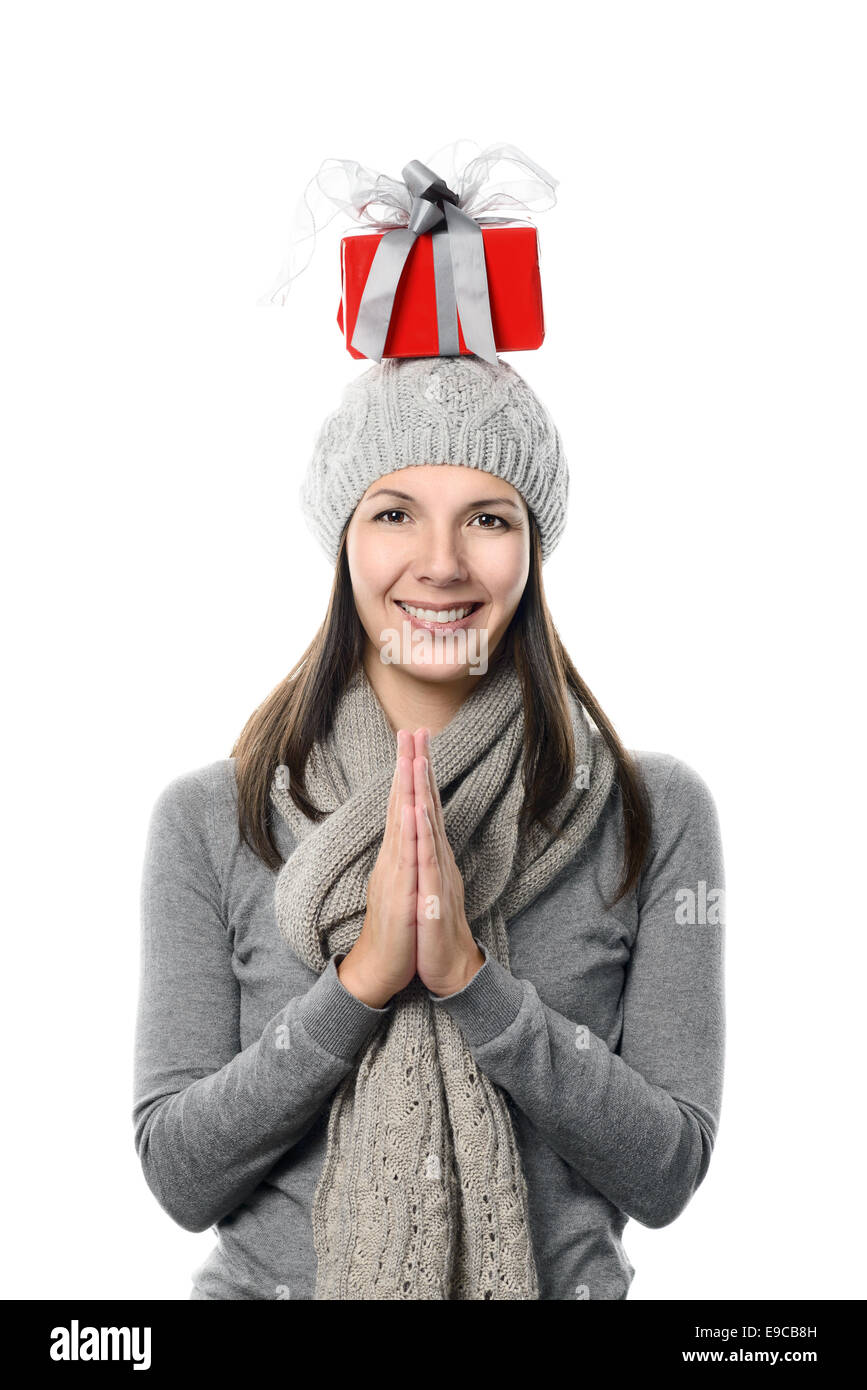 Glücklich attraktive junge Frau in Wintermode Ausgleich ein Weihnachtsgeschenk auf ihrem Kopf stehend in die Kamera schaut Stockfoto