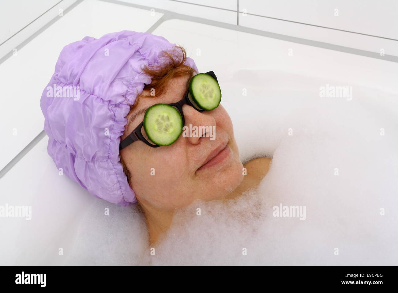 Reife Frau in der Badewanne mit Gurkenscheiben auf das Spektakel, Verfahren Stockfoto