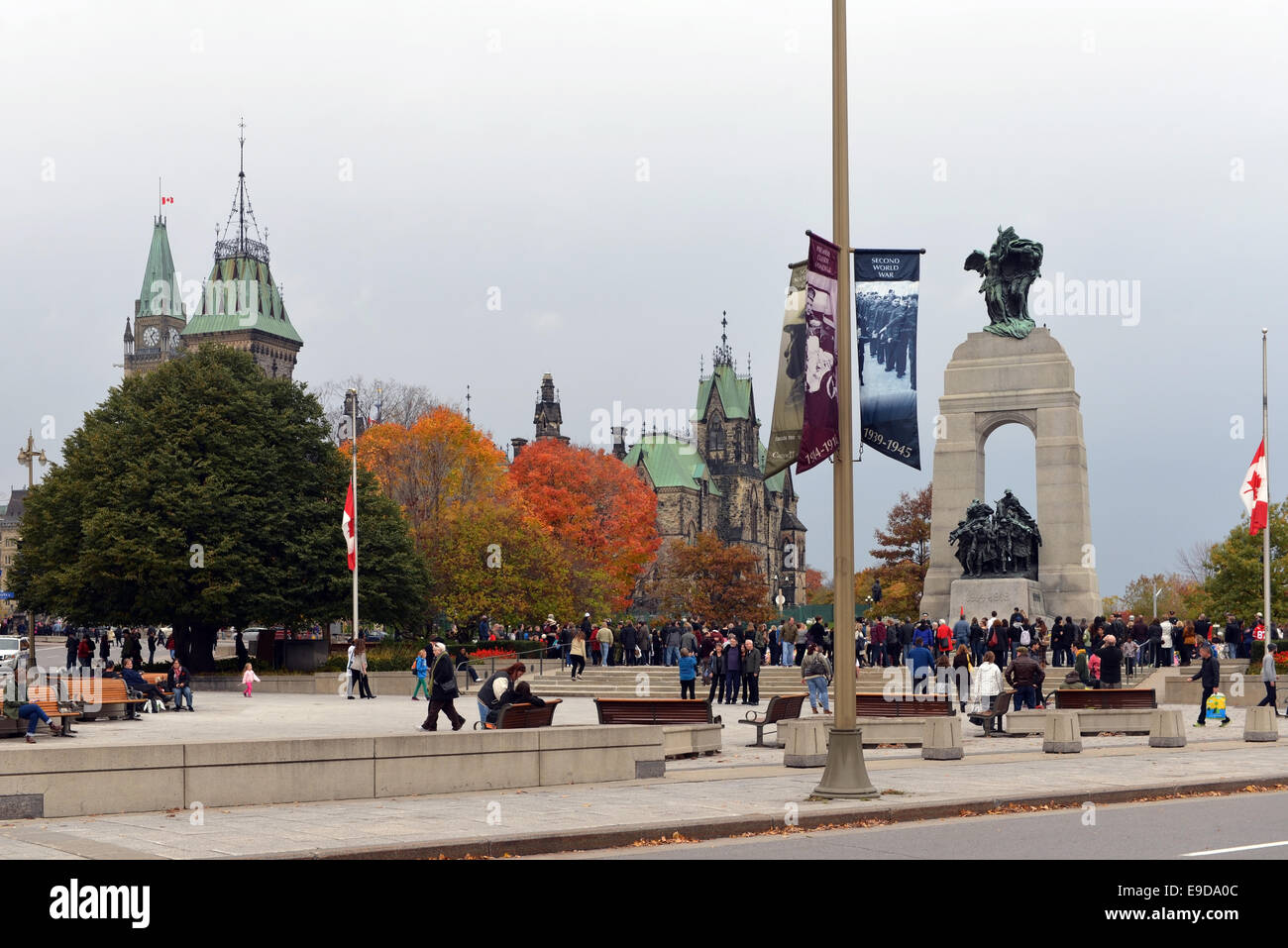 Ottawa, Kanada. 25. Oktober 2014. Trauernden sammeln und lassen Sie Blumen am Cenotaph in Ottawa, die Website wo Wache Nathan Cirillo 3 Tage bevor Sie erschossen wurde.  Die Nähe zu der Peace Tower of Parliament Hill, mit der Fahne auf Halbmast, ist auf dem Bild sichtbar. Bildnachweis: Paul McKinnon/Alamy Live-Nachrichten Stockfoto