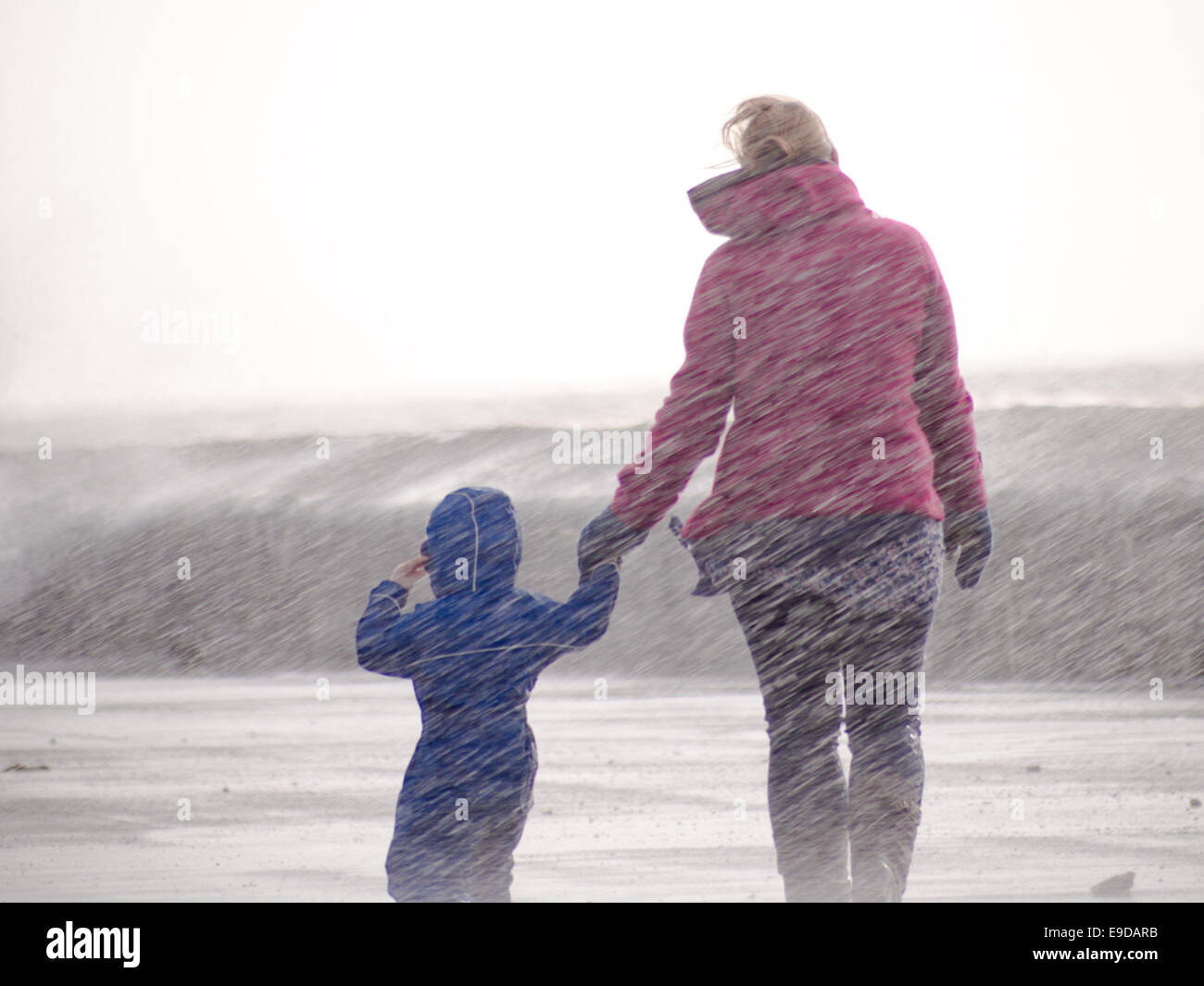 Eine Mutter und Kind zu Fuß am Meer sind durch eine Welle bricht über den Deich gefangen. Stockfoto