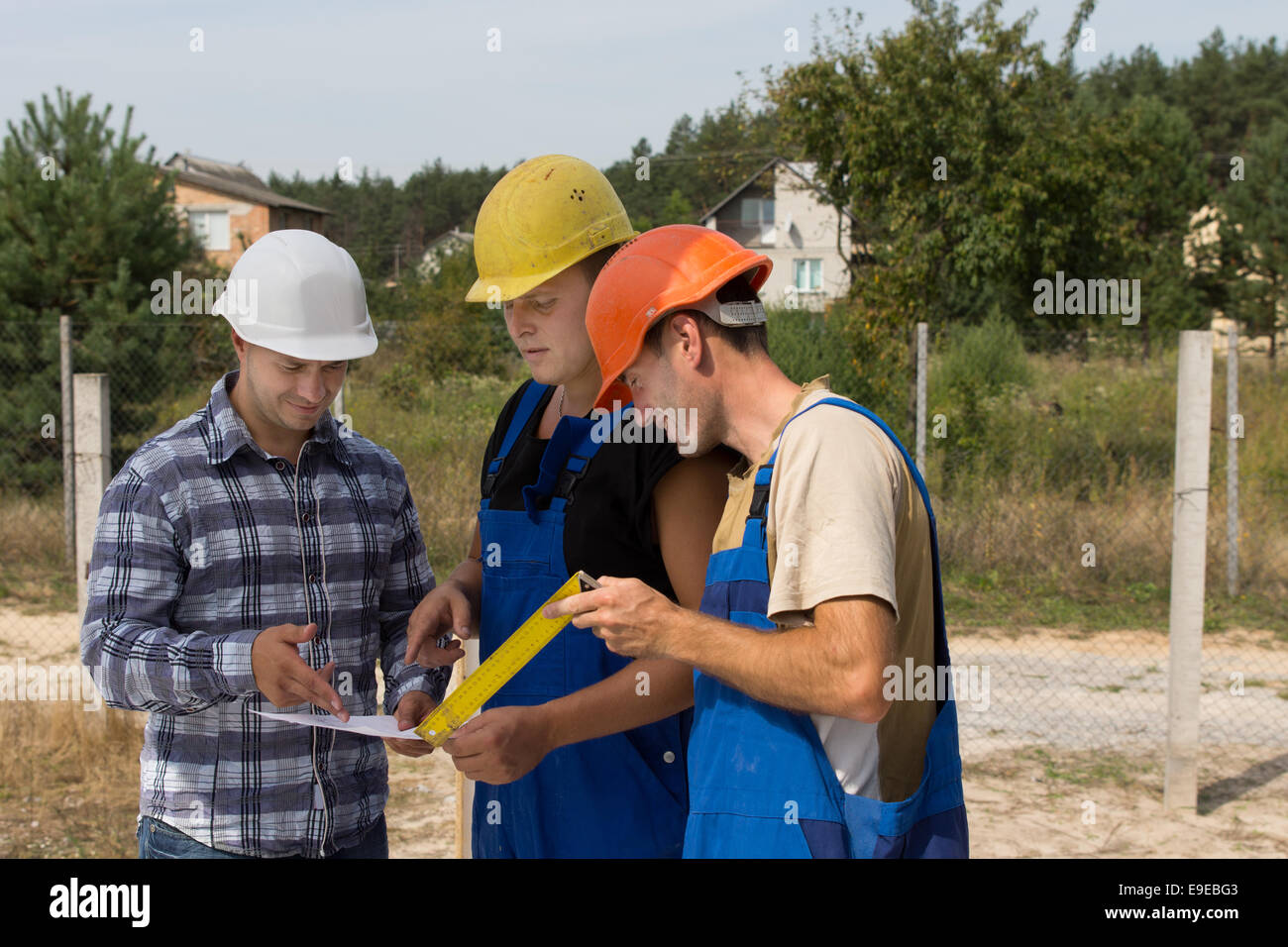 Drei Bauherren in ihre Schutzhelme stehen in einer Gruppe, die Unterlagen auf der Baustelle zu diskutieren, wie sie versuchen, ein Problem zu lösen Stockfoto