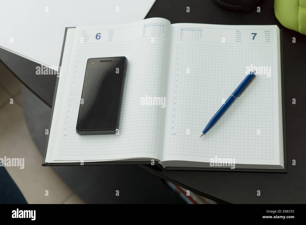 Moderne Handy- und blauen Stift auf sauberen Notebook auf schwarzen Tisch. Stockfoto