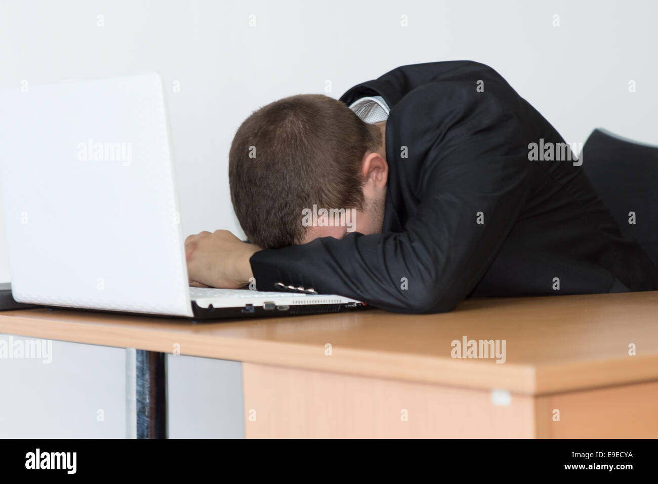 Müde junge Büro Mann im schwarzen Anzug ein Nickerchen auf seinem Schreibtisch vor seinem Computer. Stockfoto