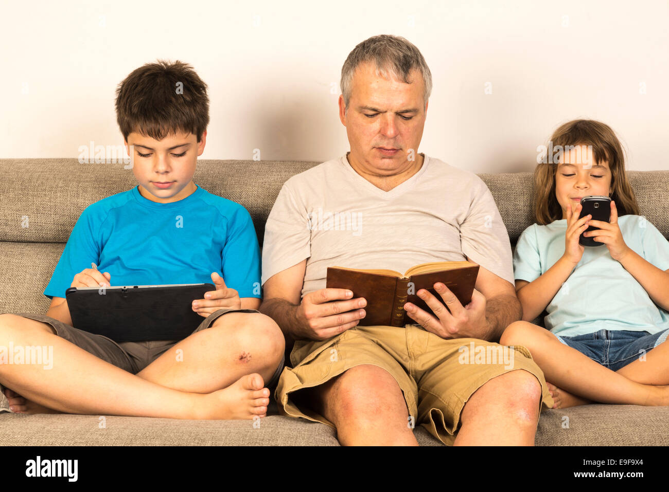 Vater und Kinder sitzen auf dem Sofa lesen oder spielen Stockfoto