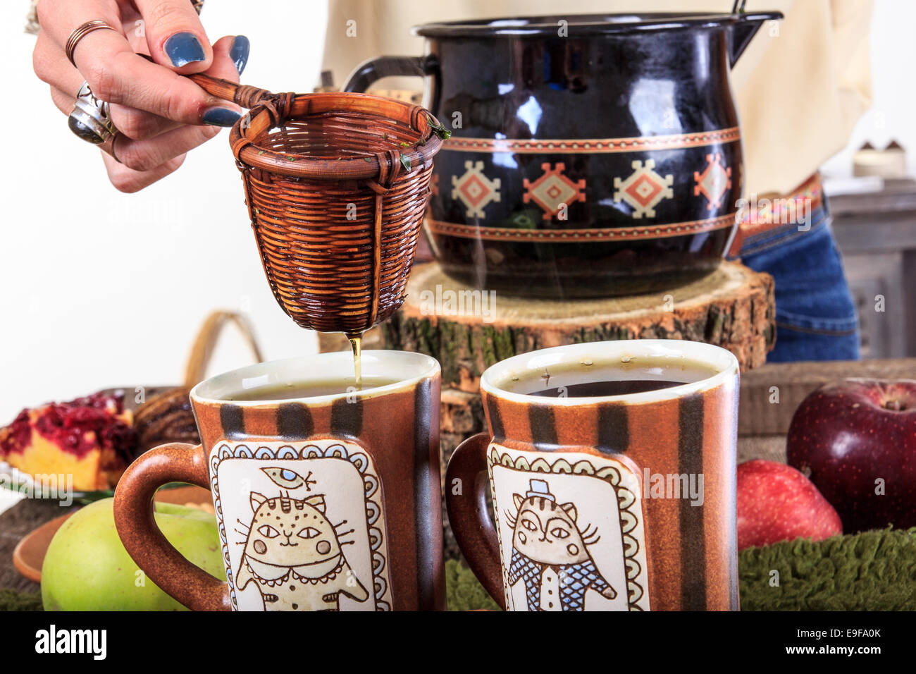Womans Hand Gießen aus Teetasse für den Tee durch ein Sieb in zwei Tassen Tee, einen angenehmen Herbst Dekoration mit Früchten und c Stockfoto