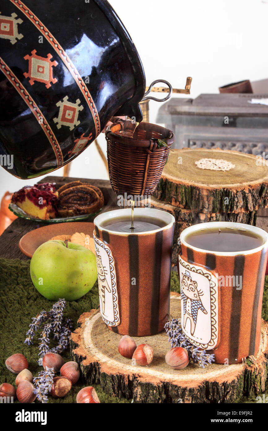 aus den Wasserkocher für Tee Gießen durch ein Sieb, in zwei Tassen Tee, einen angenehmen Herbst Dekoration mit Obst und Kuchen Stockfoto