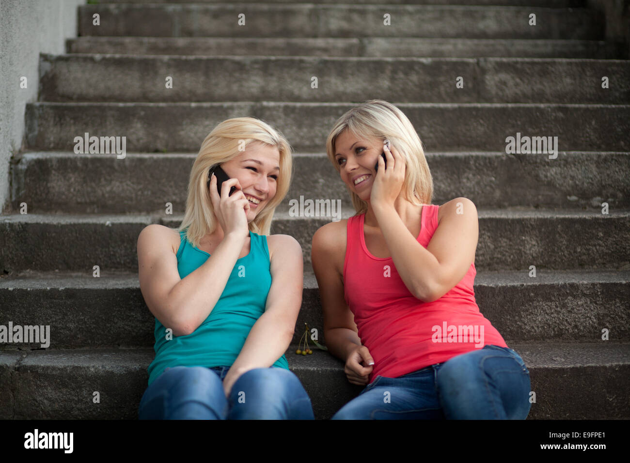Zwei Mädchen sitzen auf den Stufen mit Telefonen und reden, Spaß Stockfoto