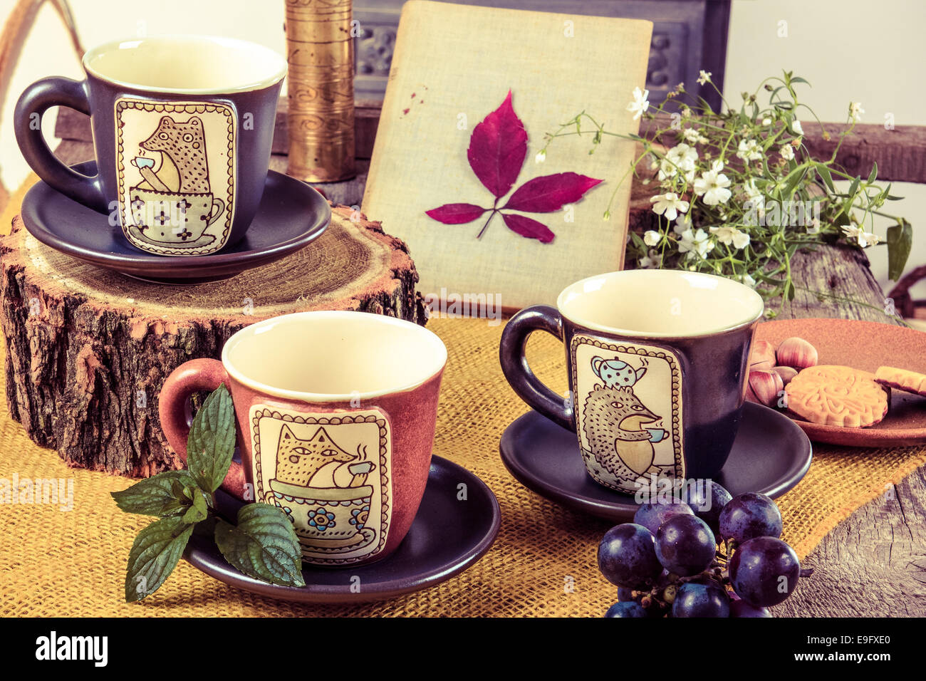 drei leere Becher für Tee auf Retro-Holztisch neben der Rinde eines Baumes mit Cookies und Traube neben Stockfoto