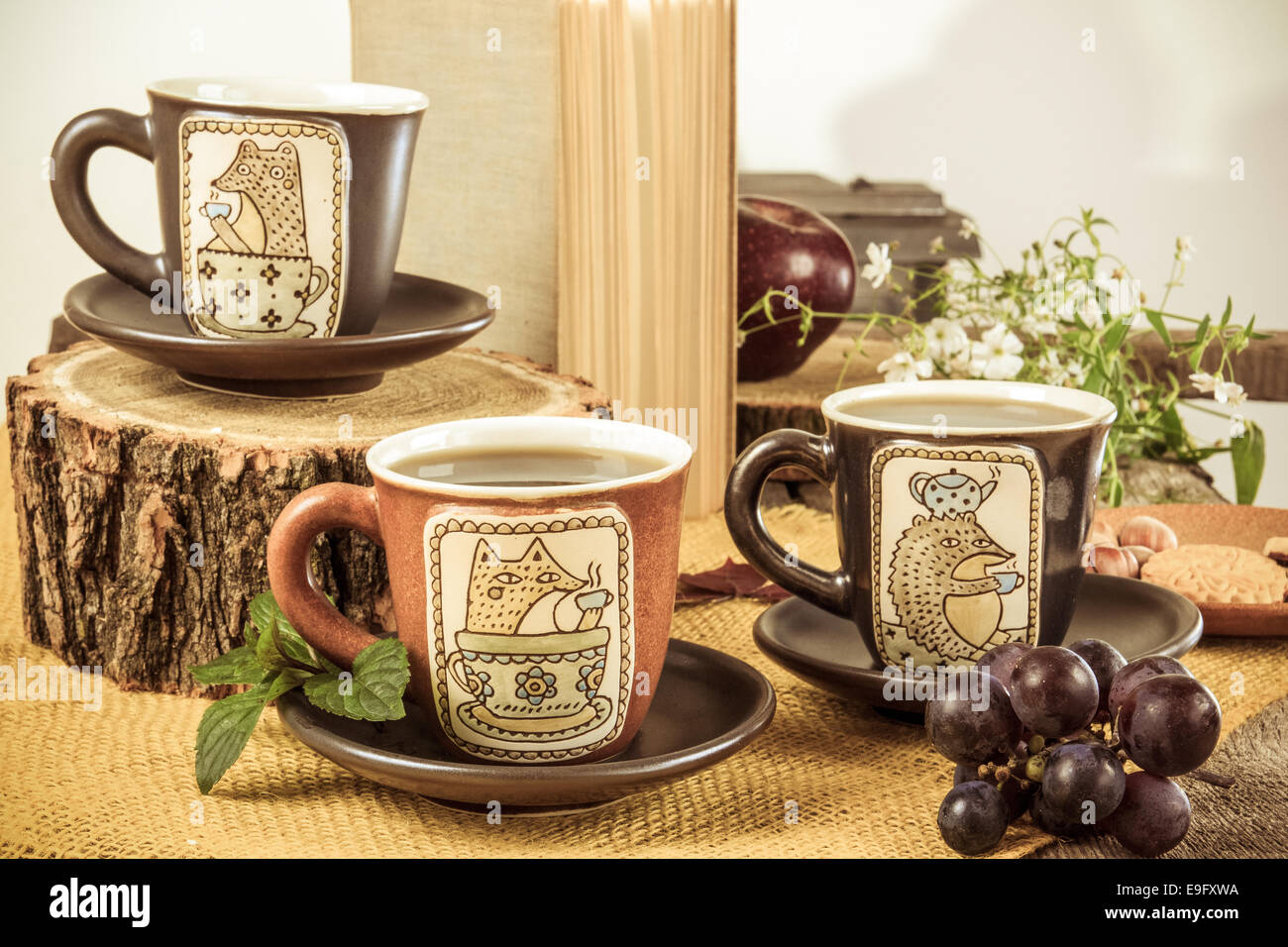 drei Retro-leere Becher für Tee auf Retro-Holztisch neben der Rinde eines Baumes mit Cookies, weiße Blume und Traube neben Stockfoto
