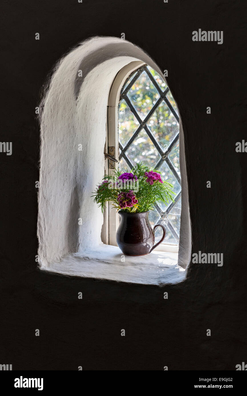 Cotehele, Saltash, Cornwall, Großbritannien. In einem kleinen mittelalterlichen Fenster steht ein einfacher Krug aus Steingut mit Schnittblumen Stockfoto