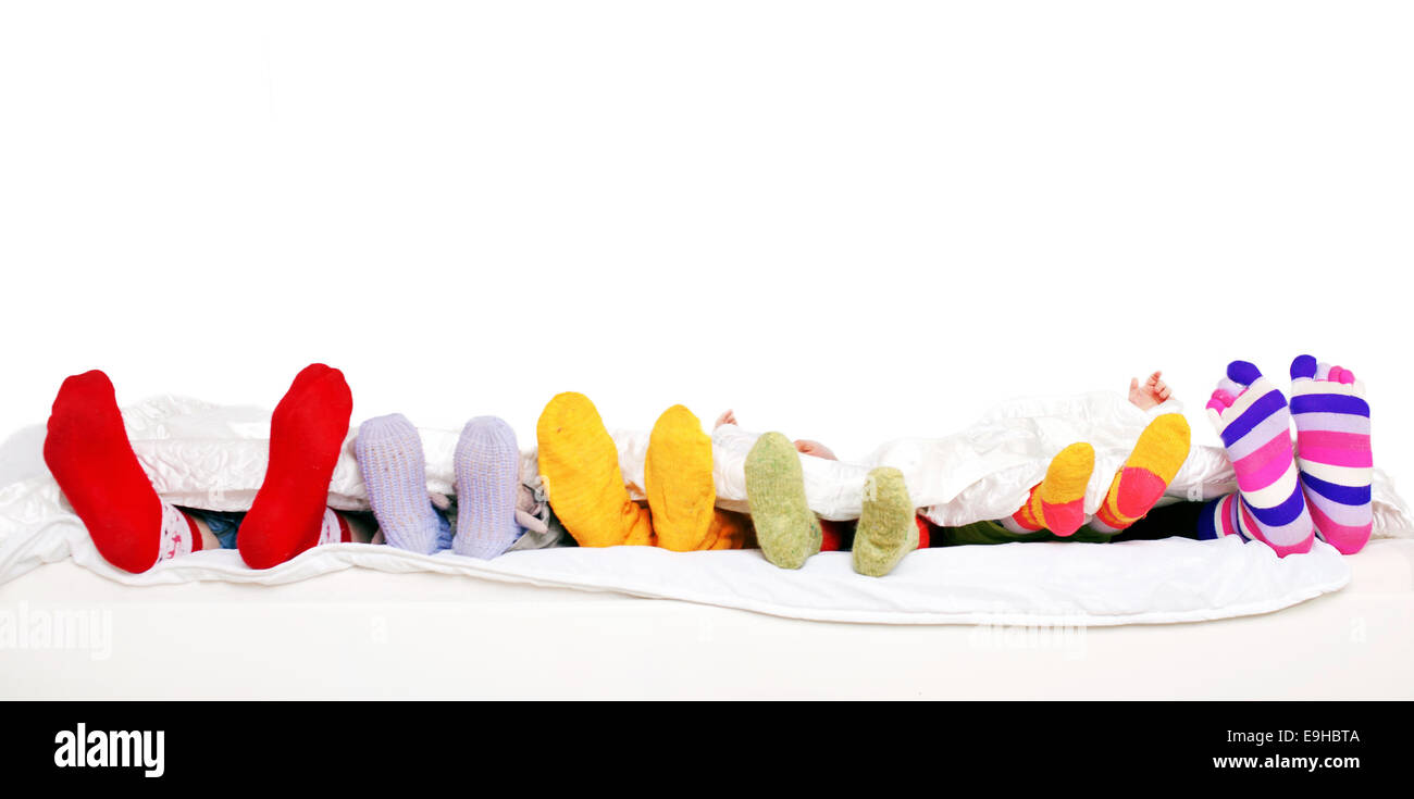 Familie miteinander schlafen. Füße aus Vater, Mutter und vier Kindern in bunten gestrickten Socken auf weißen Bett. Isoliert auf weißem bac Stockfoto
